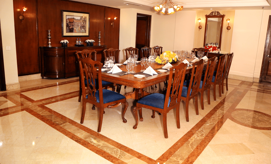 Private dining room at The Bristol Hotel, Gurgaon with a long wooden table, blue upholstered chairs, place settings, and a yellow floral centrepiece.