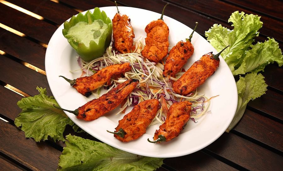 A plate on a wooden table features several pieces of tandoori-style sweet peppers, garnished with shredded cabbage, lettuce leaves, and a green bell pepper filled with a light green sauce at Uday Samudra Leisure Beach Hotel.