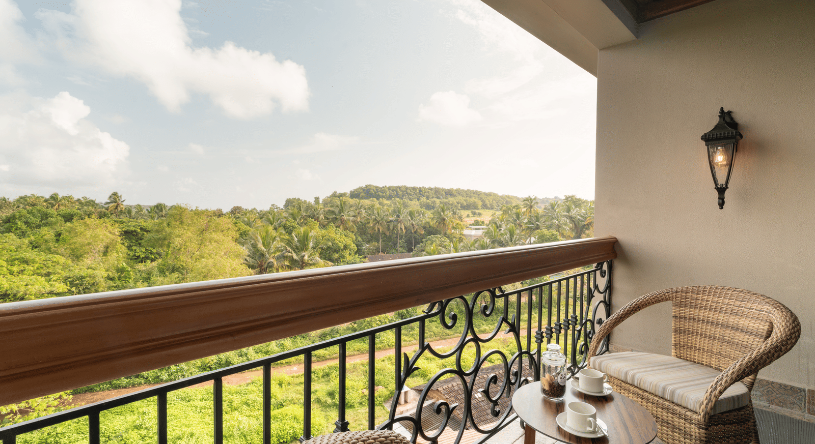 An expansive balcony with 2 arm chairs and a coffee table overlooking at the lush green lawn from the Classic Room (Diwa) at The Evren, Vagator.