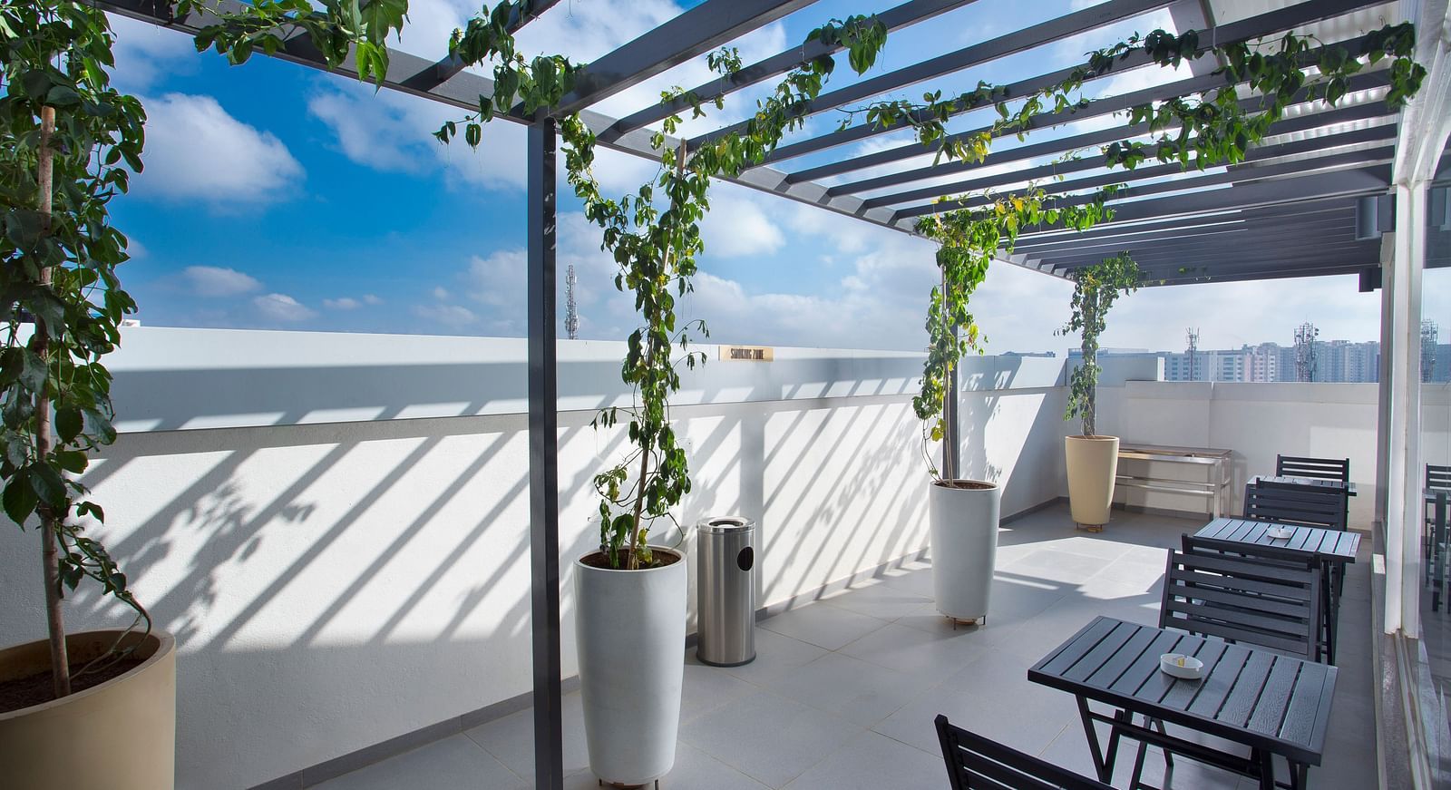 A rooftop terrace with a pergola, climbing plants and seating area against an urban backdrop - De Venetian by TGI, Brookefield