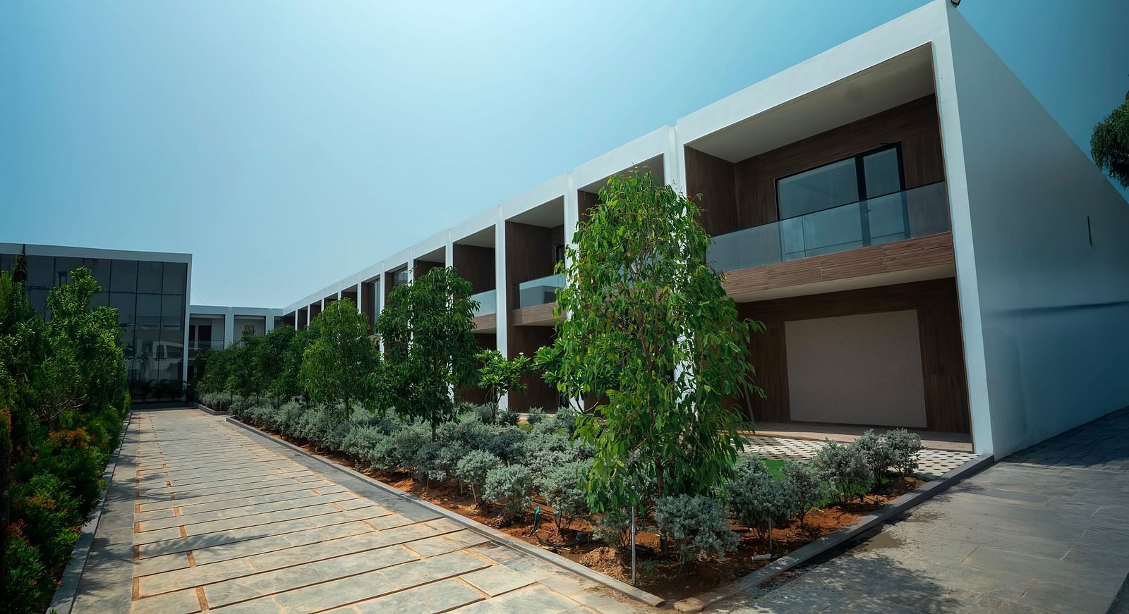 Corner view shot of a two storey building with tropical plants lined in front of it besides a pathway at The Shore Trishvam, Pondicherry.