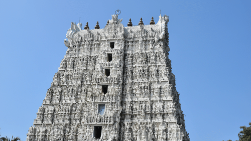 A tall, elaborately decorated temple tower with multiple tiers, set against a clear blue sky.