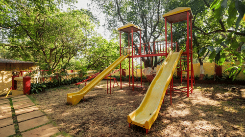 Outdoor children's play area with slides set under large trees at Adamo The Village.