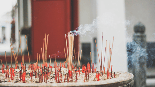 Incense sticks burning in a pot, releasing smoke, symbolising a peaceful and spiritual atmosphere in a place of worship.