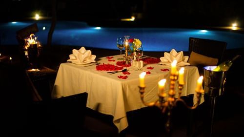 Beautiful table set up with candle lights and rose petals near swimming pool