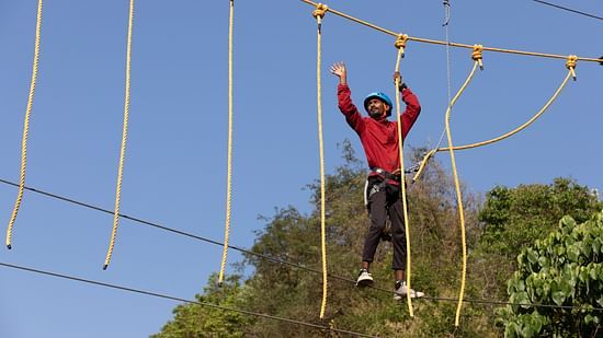 Person navigating a high rope course under a clear blue sky. | Stone Wood Jungle Resort, Dandeli