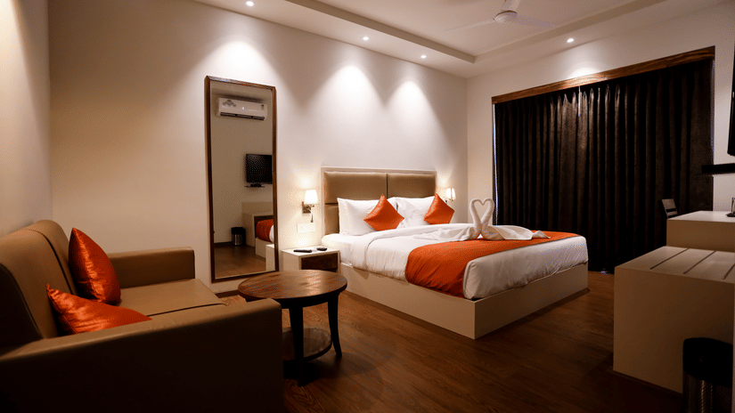 A room with a double bed, a seating area, and a mirror beside it at Amara Grand Baga, Goa.