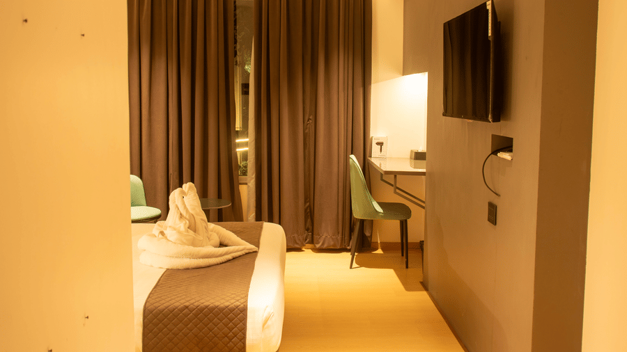 A bedroom with a king size bed, wall-mounted TV, work desk, chair, and folded towel decor at Magnus Lxia Premier, Kalyani Nagar.