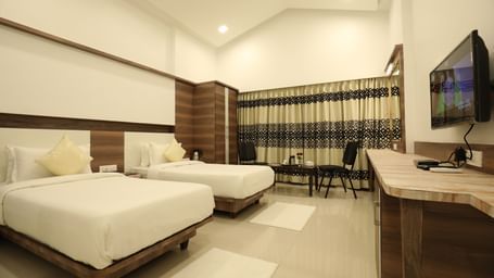 A room in Imperial Grande with twin beds, featuring a wall mounted television, and a large window with its drapes closed.