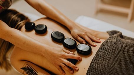 A therapist performing a hot stone massage on a patient's back, gently placing the heated stones along the spine.