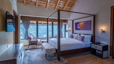 Bedroom with a four-poster bed, bedside table, and large windows offering a view, and a desk positioned below a wall-mounted television at The Chamomile Estate.