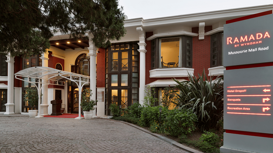 A multi-storey building exterior features a main entrance and a signage board for Ramada by Wyndham Mussoorie Mall Road.