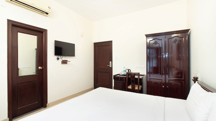 Hotel room with an air conditioner, a dark wooden wardrobe, a television, and a wooden door at Sanctum Suites Indiranagar, Bangalore.