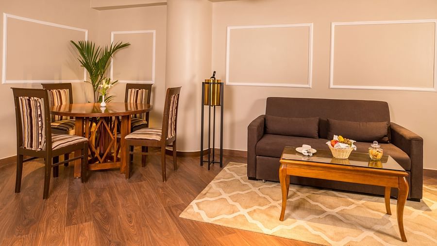  U-shaped cushion sofa with a table featuring tea pots and cups on a tray, with a dining table and chairs to the left side.