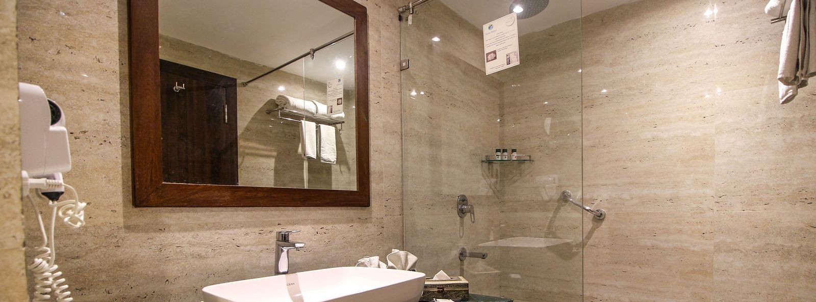 A modern bathroom with a glass shower, a sink on a dark counter, and a large mirror. - Bamboo Saa Resort & Spa, Udaipur