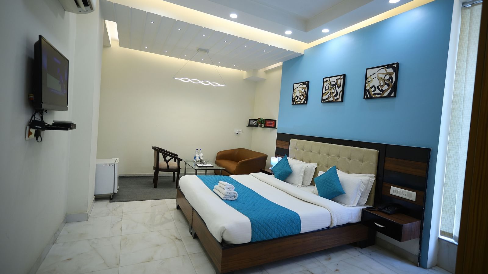A room with two single beds featuring blue and white bedding, a television, and framed artwork on the wall - Asian Suites Cyber Park, Gurgaon