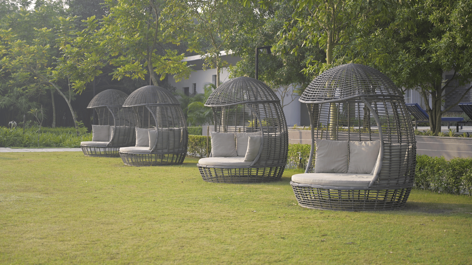 Outdoor cocoon-style seating pods arranged on a grassy lawn surrounded by trees at Hotel Sonar Bangla Mayapur.