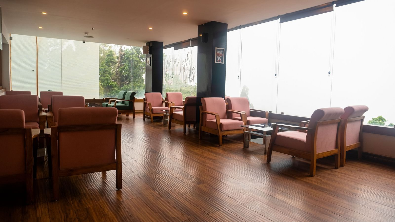 A wide shot of a spacious room with polished wooden floors, large windows, armchairs, and small tables at Orsino Spa Resort.