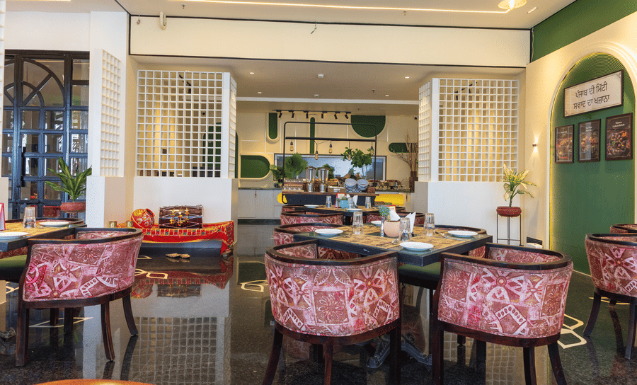 Restaurant interior at Hotel Bawa, Udaipur displaying square dining tables, patterned armchairs, white lattice partitions, and a low seating area.