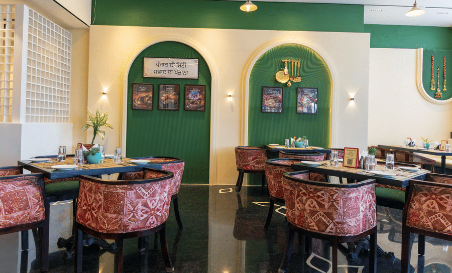 Restaurant dining area at Hotel Bawa, Udaipur featuring square tables, patterned armchairs, arched wall alcoves with pictures, and wall sconces.