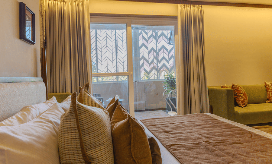A lit bedroom with a king size bed, sheer curtains and direct access to a private balcony at Hotel Bawa, Udaipur