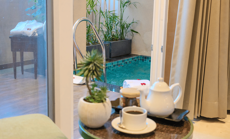 Private plunge pool surrounded by lush green plants with a tea set placed beside it in the Royal Suite at Hotel Bawa, Udaipur.