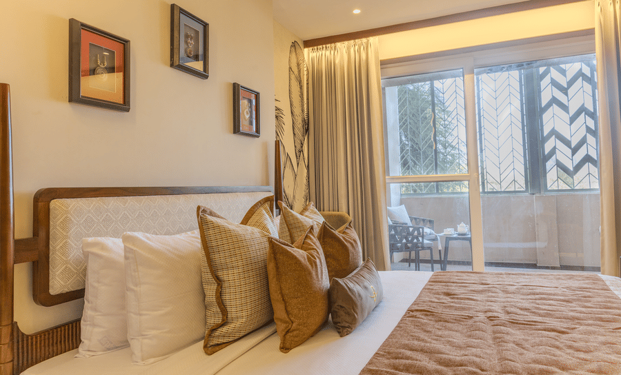 Bright bedroom with a king size bed, mustard bench, potted indoor plants and access to a private balcony at Hotel Bawa, Udaipur.