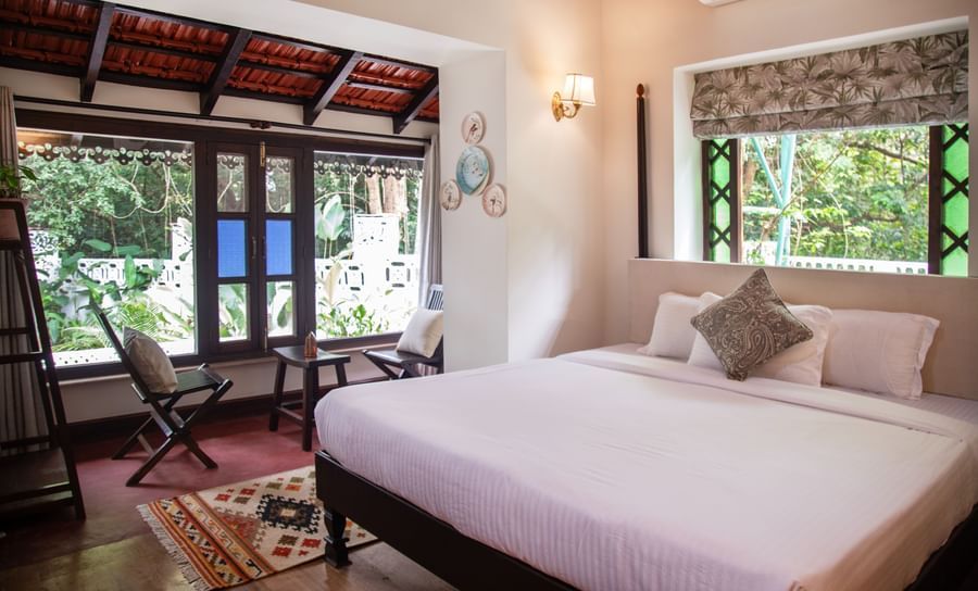 An image of a bed with big windows on the side with greenery outside at Lamrin Ucassaim Hotel, Goa