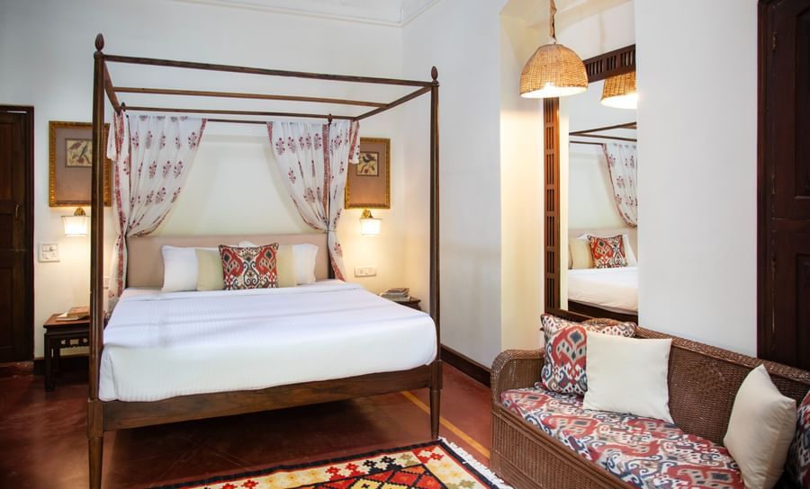 An image of a four poster bed with a sofa and bedside table on either side - Lamrin Ucassaim Hotel, Goa
