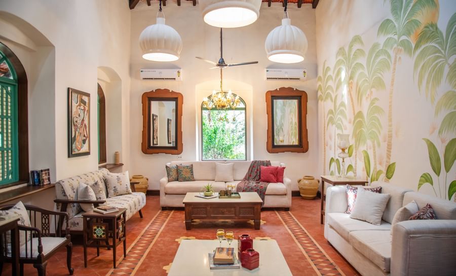 An image of a living area with sofas and centre tables, photo frames on the wall, tables on each corners where decorative items are placed at Lamrin Ucassaim Hotel, Goa