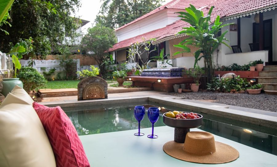 L shaped pool side with two blue wine glasses and surrounded by greenery @ Lamrin Ucassaim Hotel, Goa