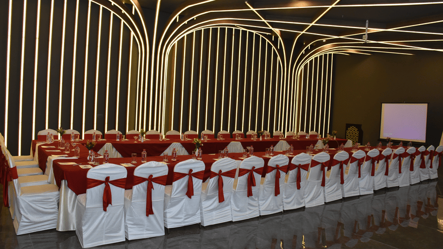 A banquet hall at Comfort Inn Sapphire by Eastlynn Collections, Jaipur with rows of chairs, tables, stage area, and ceiling lighting design.