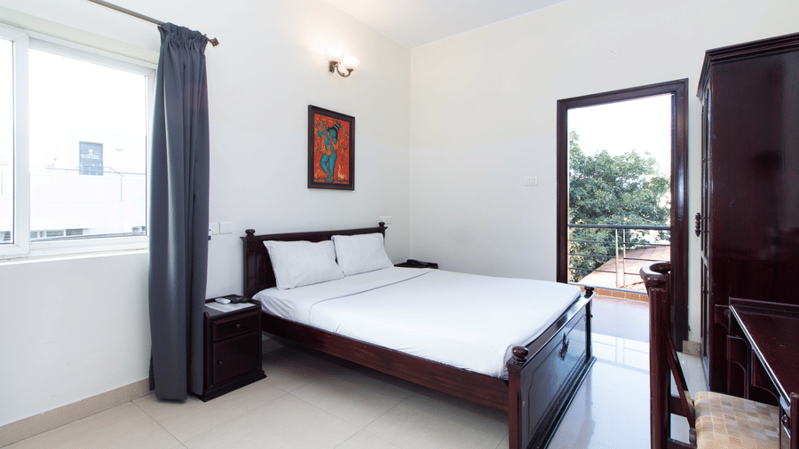 Bright hotel room with a double bed, a large window, and lush greenery views at Sanctum Suites Indiranagar, Bangalore.