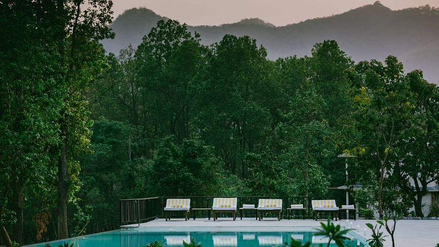A view of the outdoor swimming pool at Saraca Resort & Spa Corbett surrounded by lush trees and mountains