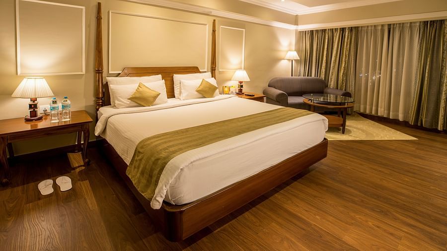 Spacious bed with a wall-mounted TV opposite it and a large window covered by curtains.