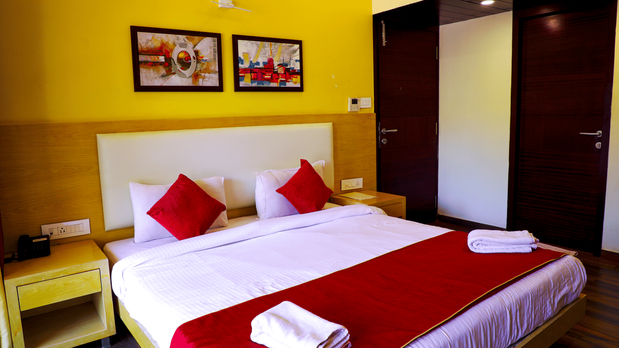 A romantically decorated hotel bed with white linens, a red runner, red accent pillows, and swan towel art surrounded by flower petals.