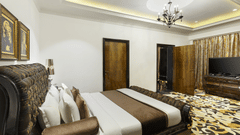 The spacious presidential suite bedroom with a king size bed, upholstered headboard, bedside tables, chandelier lighting, television unit and patterned flooring at La Marvella, Bengaluru.