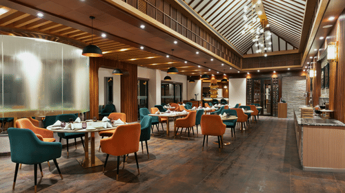 Guras Restaurant dining area at Royal Tulip Shivapuri National Park - Kathmandu with teal and orange chairs, wooden floors, and high ceilings.