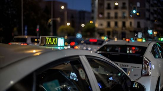 Illuminated taxi sign on top of a car in a bustling city street at dusk