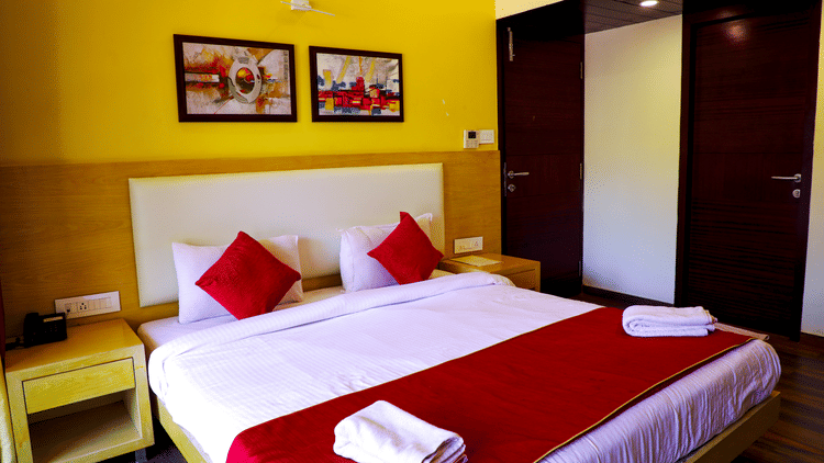 A romantically decorated hotel bed with white linens, a red runner, red accent pillows, and swan towel art surrounded by flower petals.