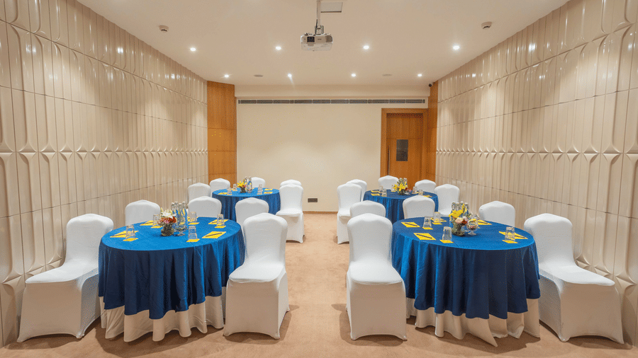 Small cluster meeting setup at Golden Tulip Jaipur City Center with round tables, blue tablecloths, white chairs, floral center pieces, and table settings for workshops and meetings.