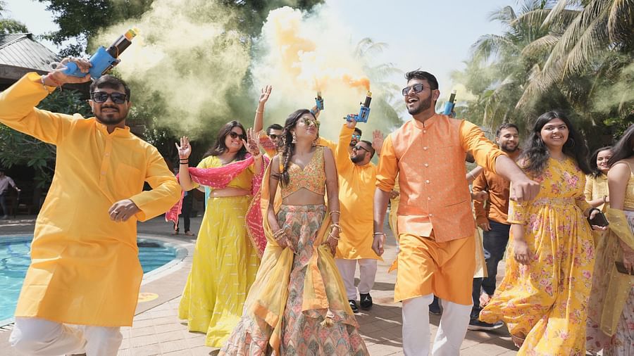 An outdoor celebration with guests dressed in bright traditional attire, holding smoke guns releasing smoke, dancing and having fun near a pool at Uday Samudra Leisure Beach Hotel