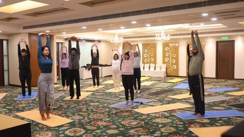 A group of people standing on their yoga mats and stretching their hands to perform yoga at Heritage Village Resorts & Spa