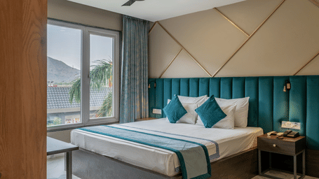 King Deluxe Room with a teal upholstered headboard and scenic mountain views at Hotel Highway King, Shahpura, offering a relaxing stay.