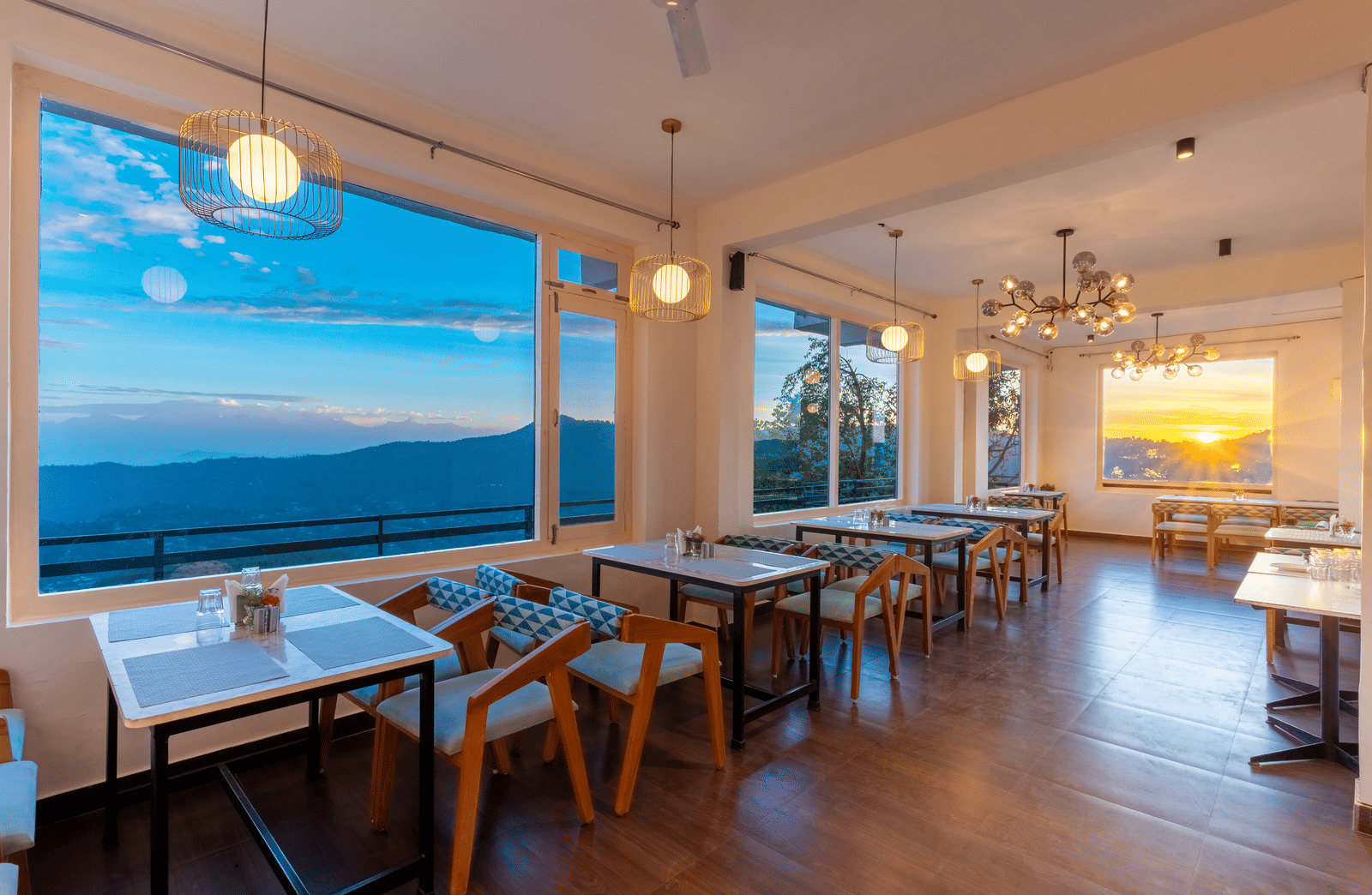An indoor restaurant area with glowing spherical lights and large windows showing the evening sky at Himalayas Resort By The Lake Hill, Mukteshwar.