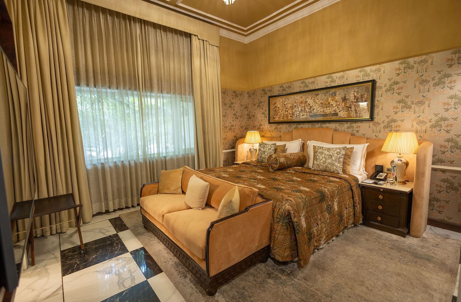 Executive Suite at The Claridges New Delhi, featuring a cosy king sized bed, a sofa placed in front, and a bedside lamp