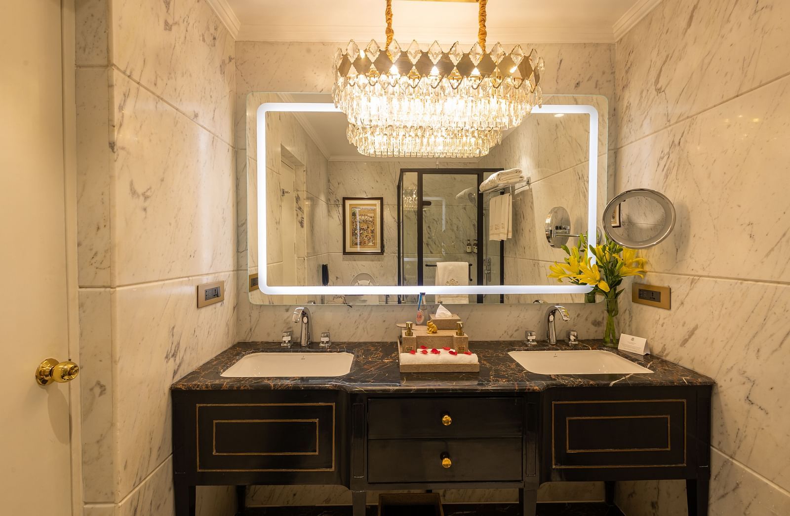Washroom of the Grand Luxury Twin Bed Room at The Claridges New Delhi, featuring sinks, a wall-mounted mirror, and an elegant chandelier hanging above