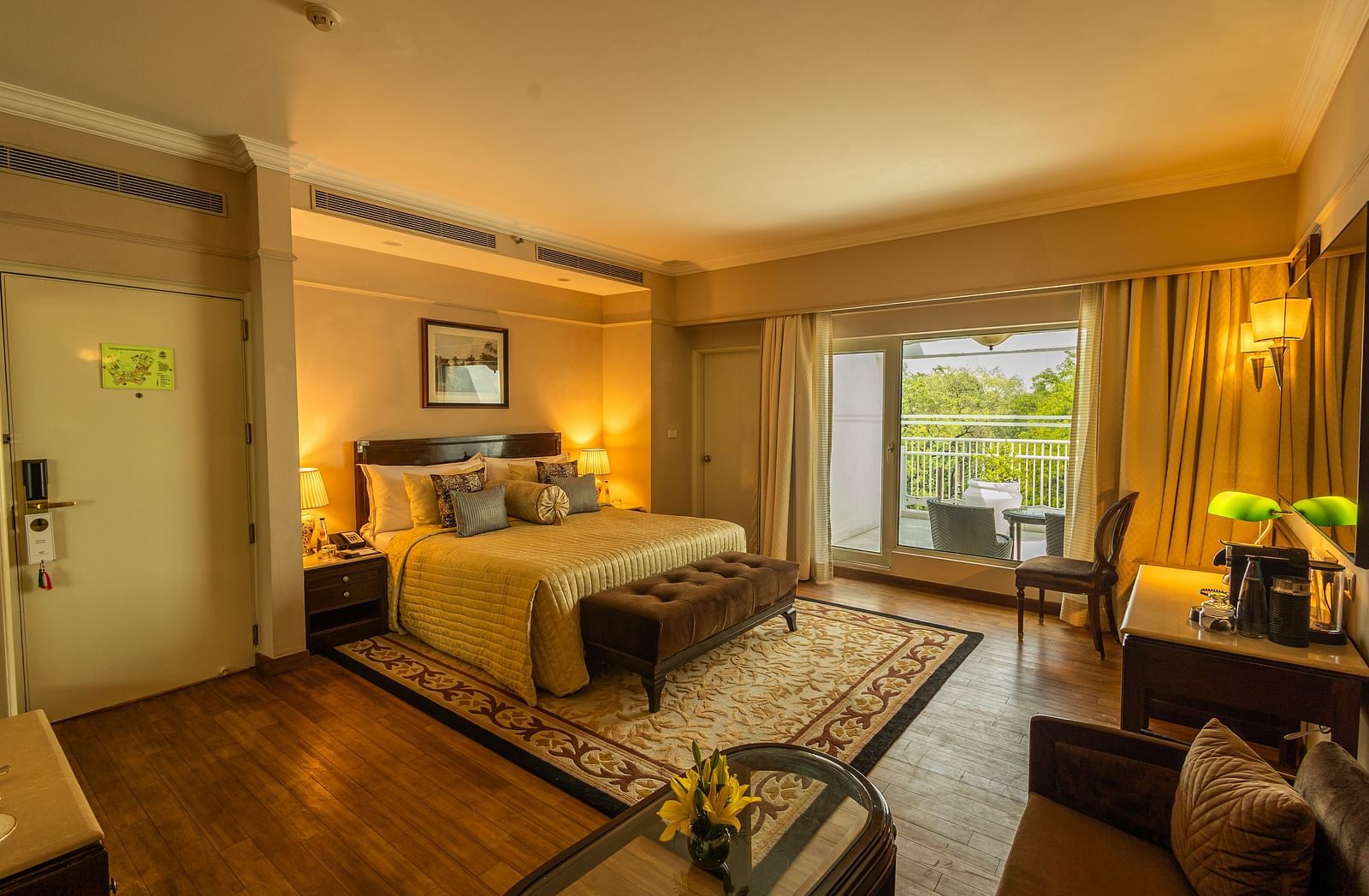 Luxury King Bed Room with Balcony at The Claridges New Delhi, featuring a cosy bed, a framed artwork on the wall, and a glass door to the balcony