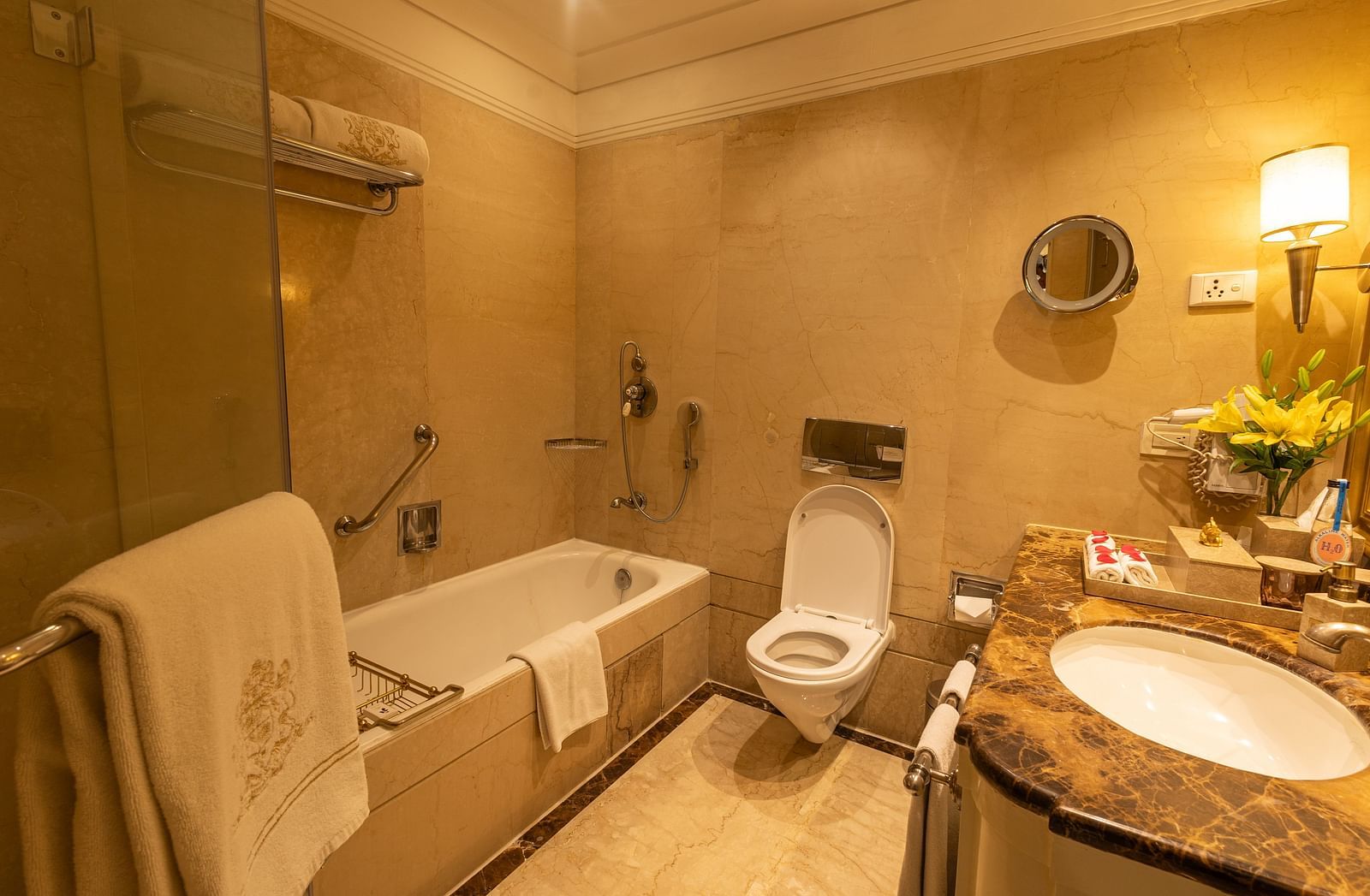 Washroom of the Luxury King Bed Room with Balcony at The Claridges New Delhi, featuring a bathtub, sleek sink, and a wall-mounted lamp in the corner