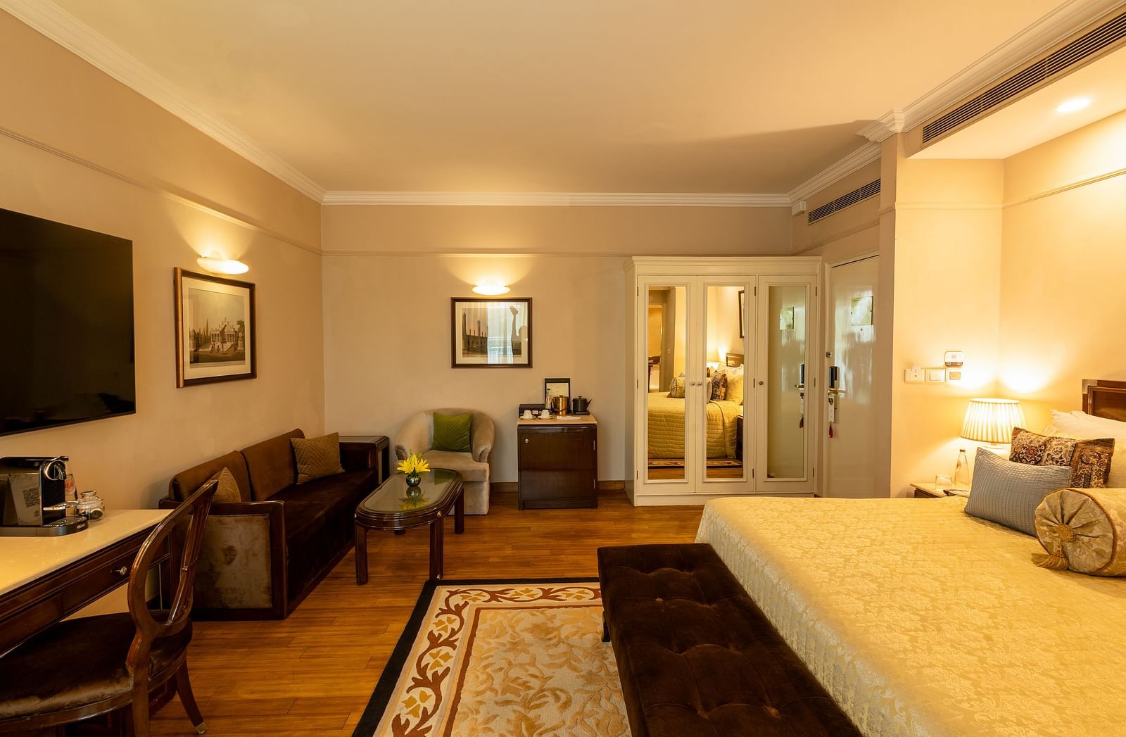 Luxury King Bed Room with Balcony at The Claridges New Delhi, featuring a plush bed, wall-mounted TV, and a cosy sofa in the corner